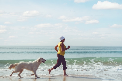 Happy elderly woman running along a beach with her golden retriever at the morning