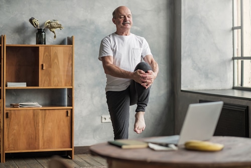 Senior handsome sportman doing stretching and balancing yoga exercise at home